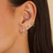 Emerald Teardrop Diamond Mini Huggie Earring in 14k yellow gold styled on first and second earring hole of model next to emerald stud earring and emerald palm tree earring