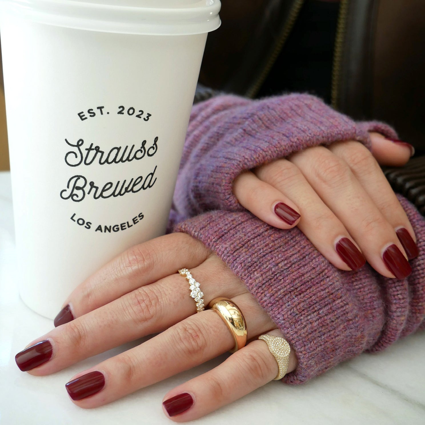 Mauve Cashmere Wrist Warmers styled on model with 14k yellow gold rings with diamonds styled on fingers next to white cup