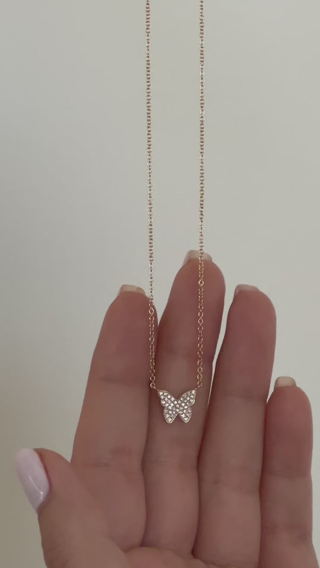 Diamond Butterfly Necklace in 14k yellow gold held in hand and then styled on neck of model wearing white blouse with no audio