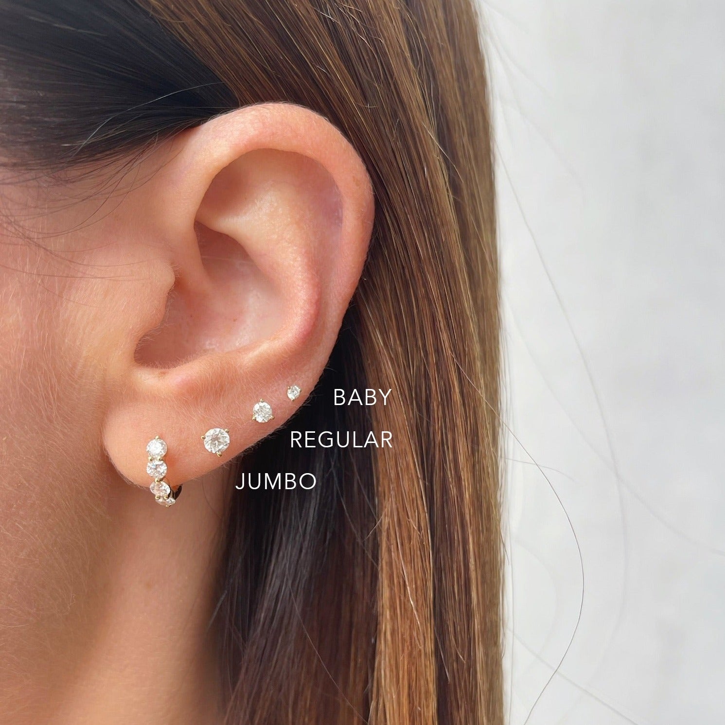 Baby Solitaire Diamond Stud Earring in 14k yellow gold styled on fourth earring hole of earlobe of model with brown hair