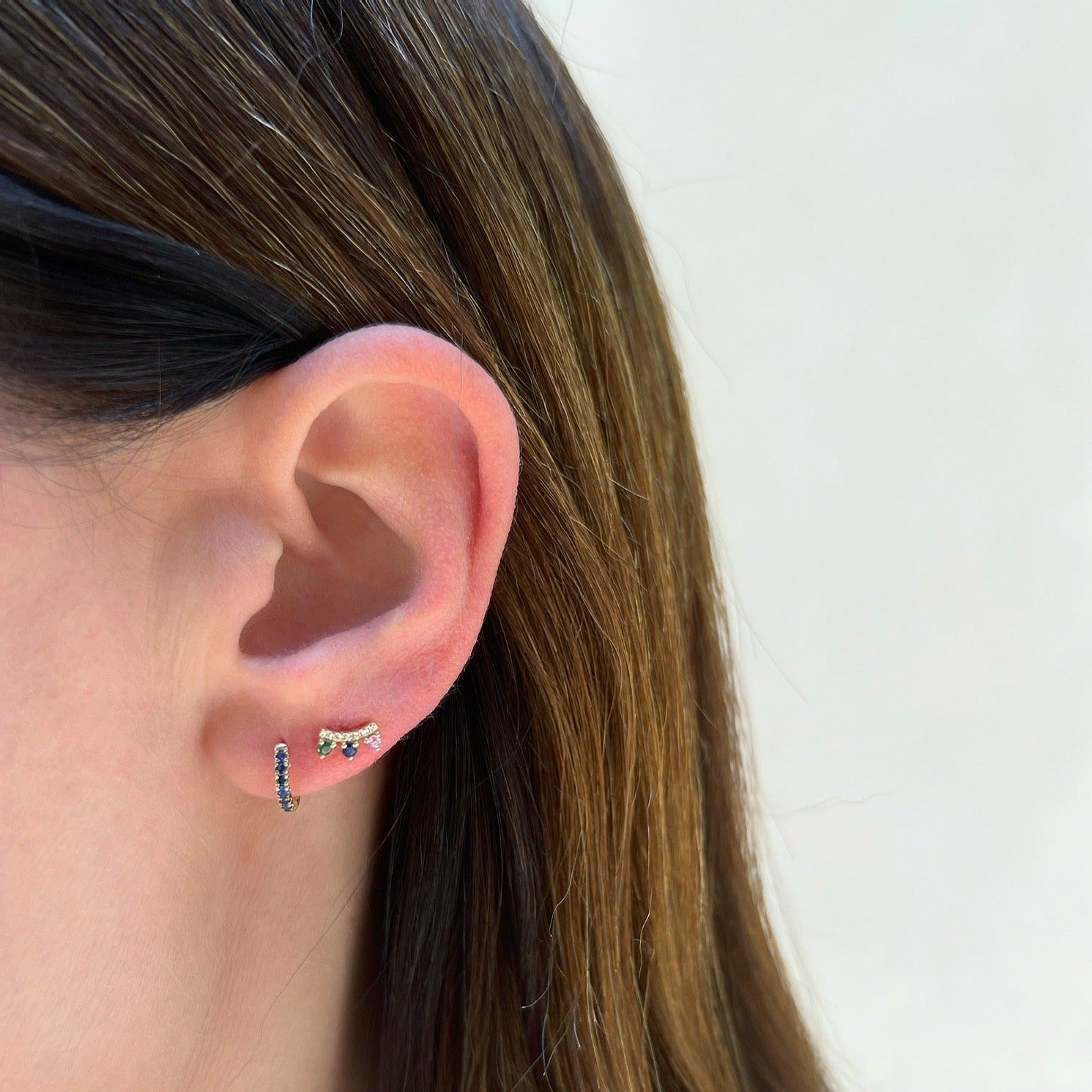 Blue Sapphire Mini Huggie Earring in 14k yellow gold on first earring hole on earlobe of model