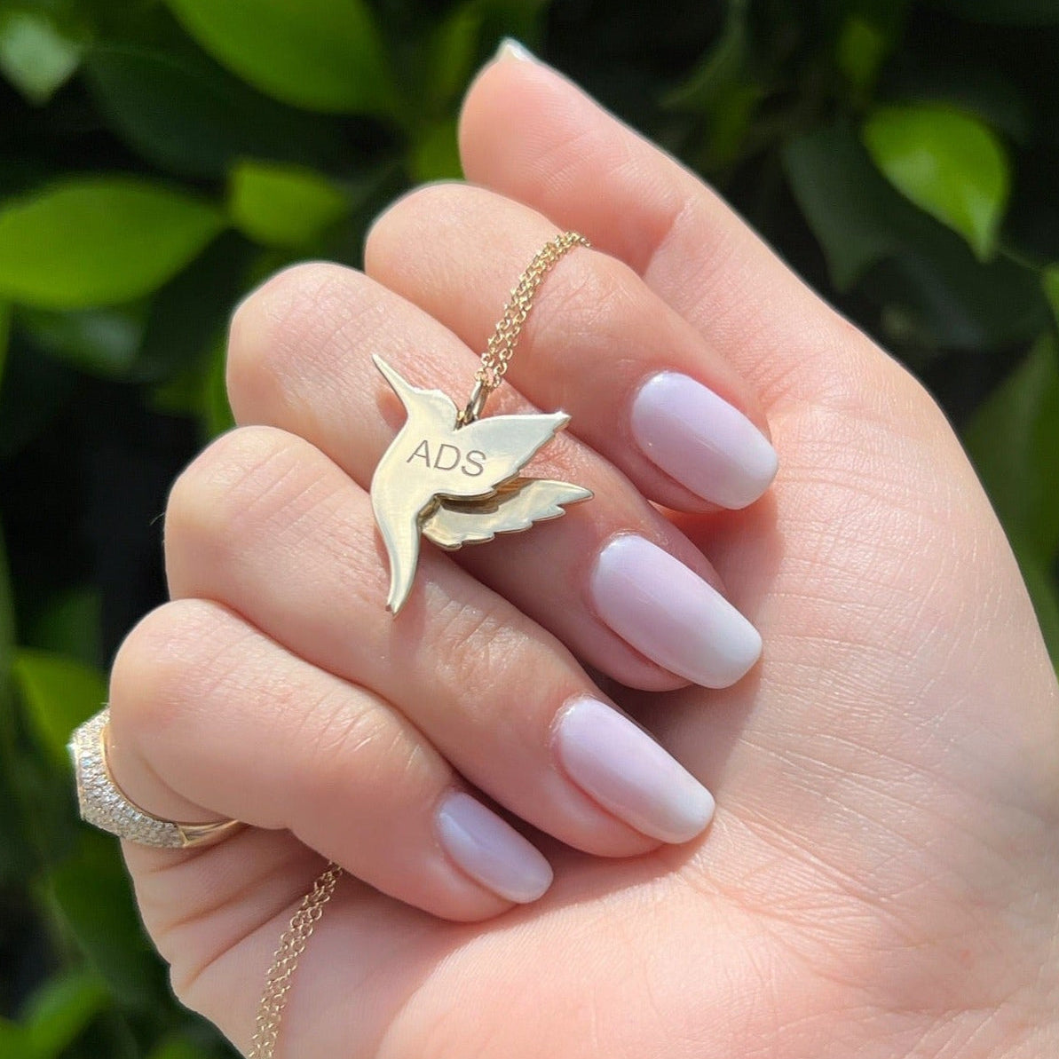 Pavé Diamond Hummingbird Necklace in 14k yellow gold with ADS engraving on back of hummingbird pendant being held in hand of model