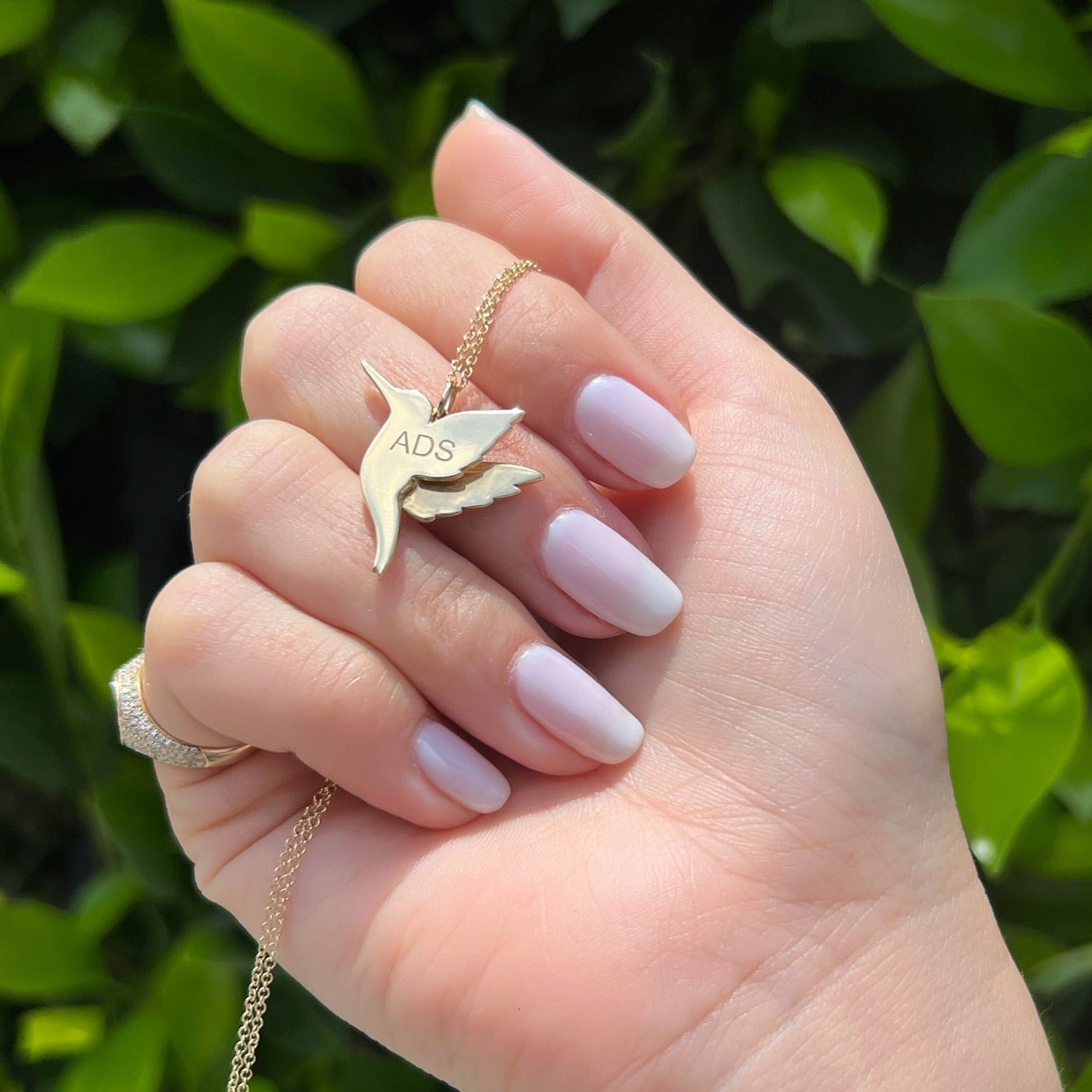 Pavé Diamond Hummingbird Necklace in 14k yellow gold with ADS engraving on back of hummingbird pendant being held in hand of model