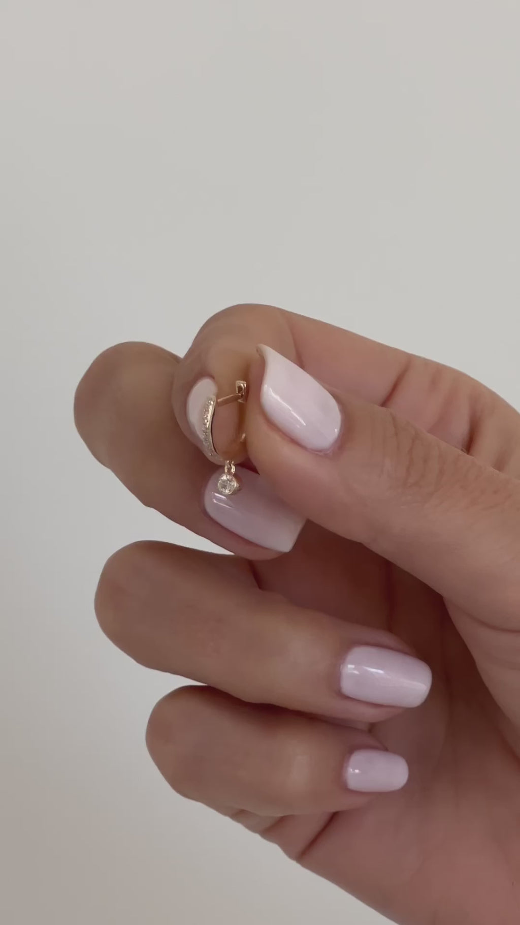 Diamond Mini Huggie With Diamond Bezel Drop Earring being held in fingers of model followed by styled on first earring hole on earlobe of model with no audio