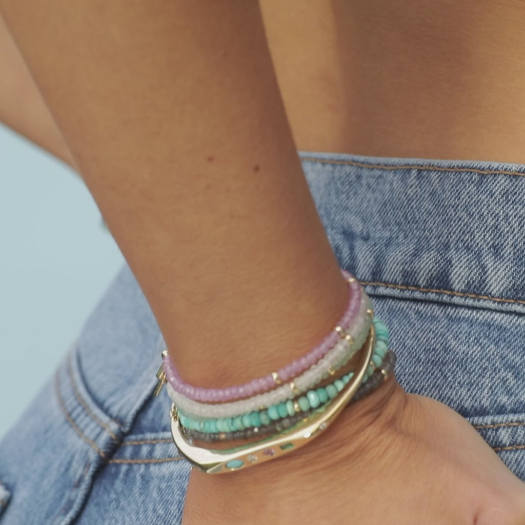 Birthstone Bead Bracelet in Labradorite styled on wrist with layered birthstone bead bracelets, gold treasure bangle and gold layered rings styled on fingers of model putting thumb in back pocket of jeans with no audio