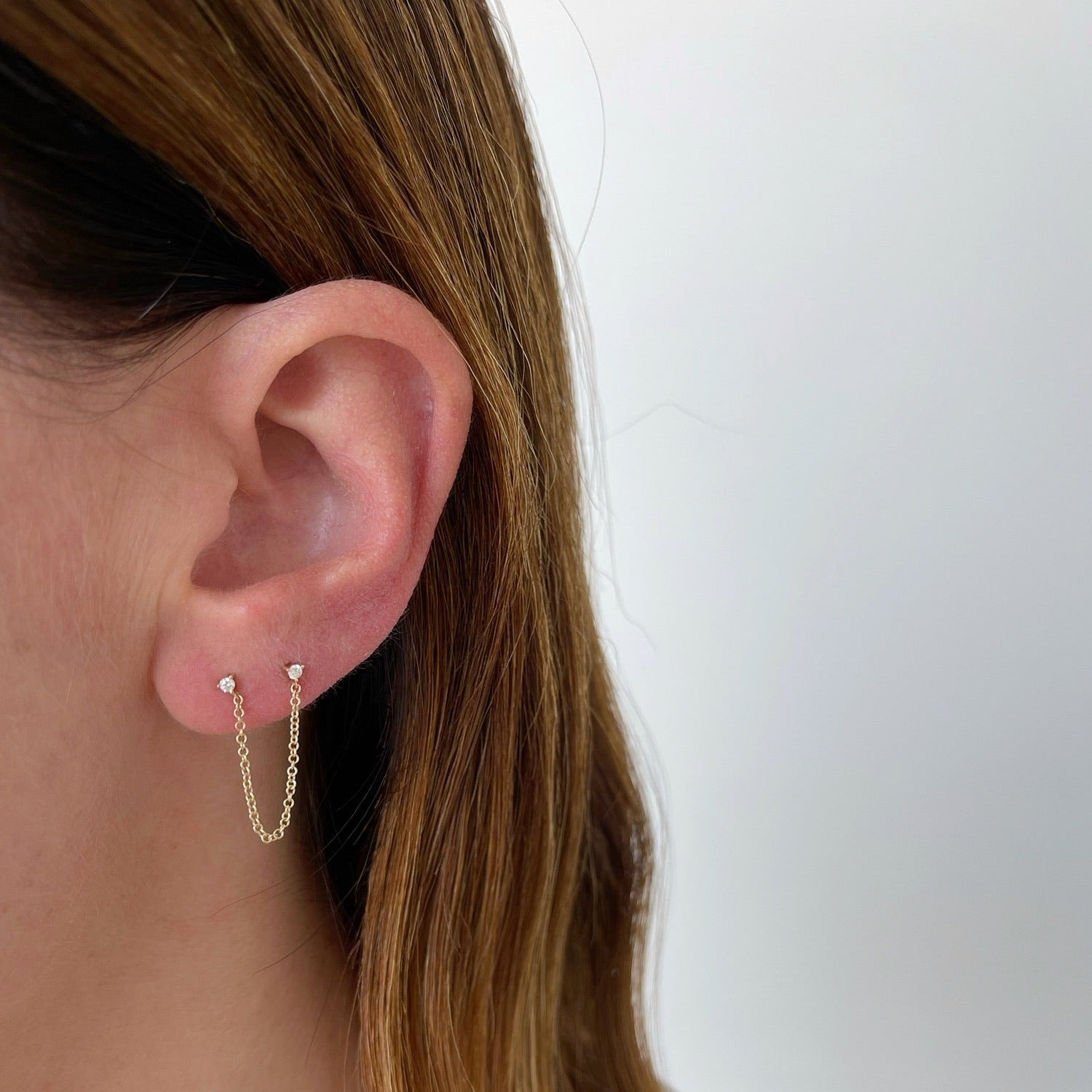 Double Diamond Chain Stud Earring in 14k yellow gold styled on ear of model with brown hair