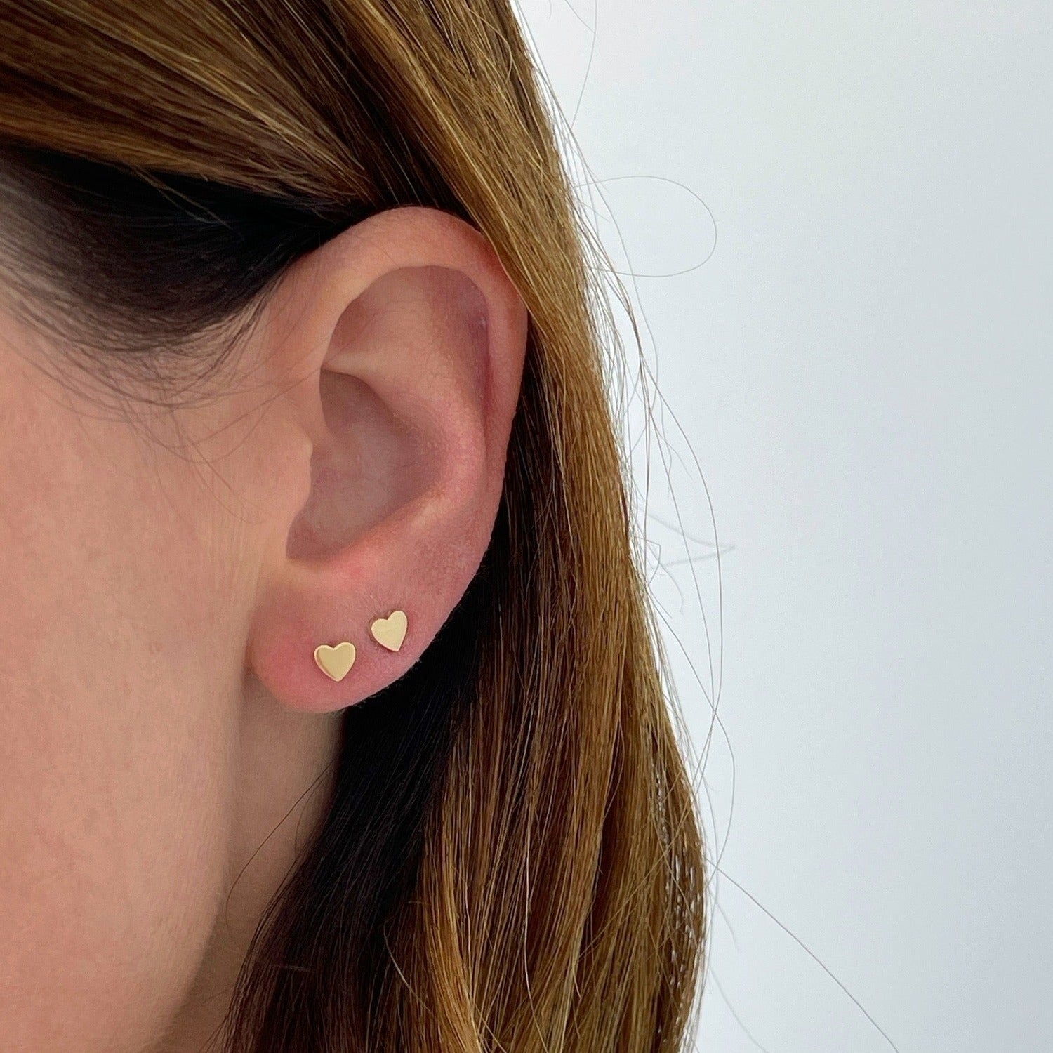 Gold Baby Heart Stud Earrings in 14k yellow gold styled on ear lobe on ear of model