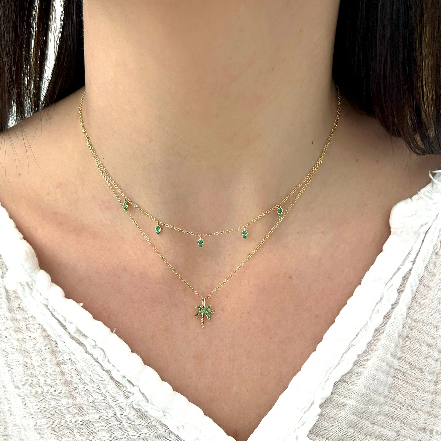 Emerald Wild Palm Necklace in 14k yellow gold styled on neck of model with 5 emerald drop necklace with model wearing white blouse