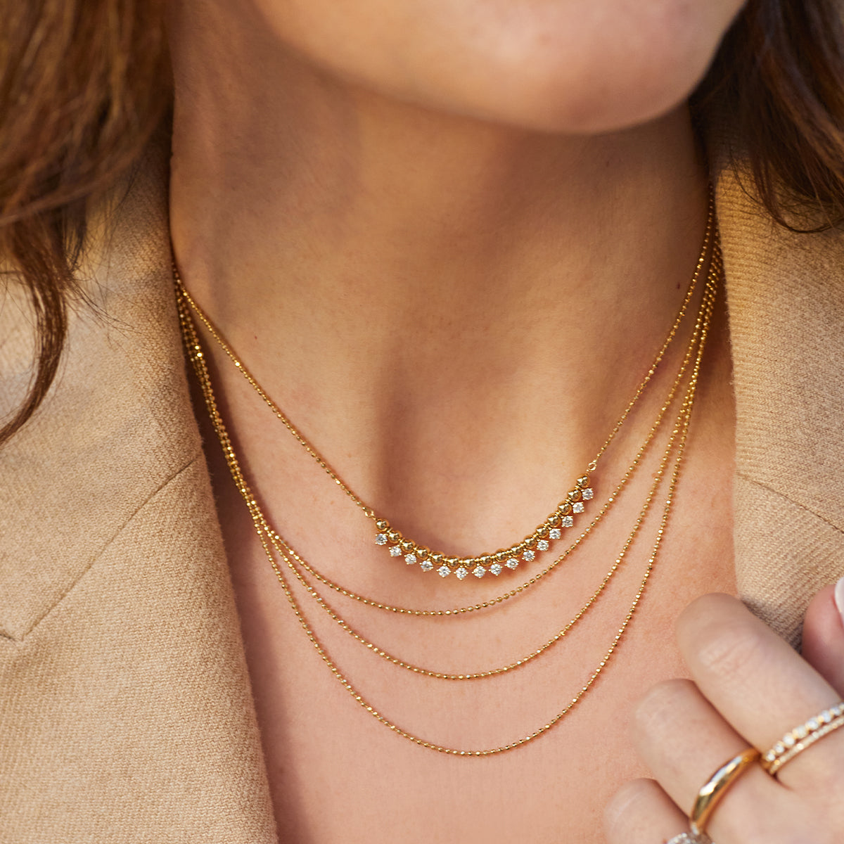 Hasson Triple Layered Chain Necklace in 14k yellow gold styled on neck of model with diamond and gold ball necklace