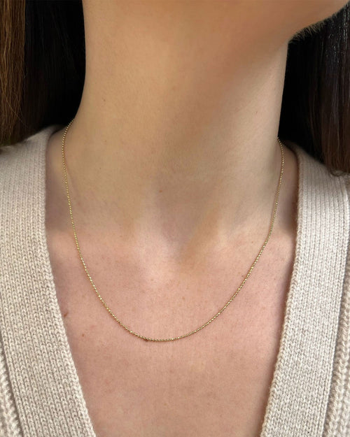 Gold Faceted Ball Chain in 14k yellow gold styled on neck of model wearing tan sweater