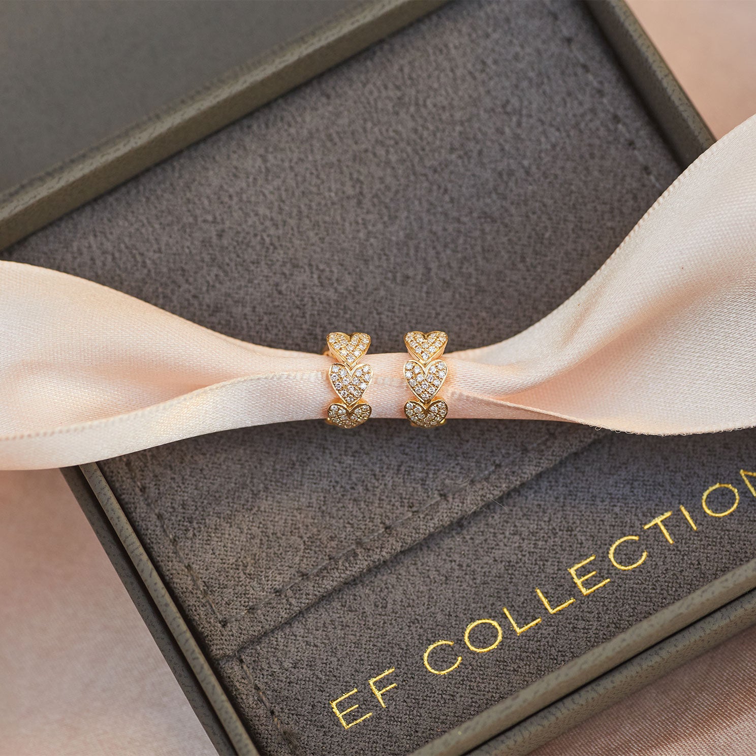 Diamond Multi Heart Huggie Earring in 14k yellow gold displayed on pink ribbon inside grey jewelry box with EF Collection logo in gold letters