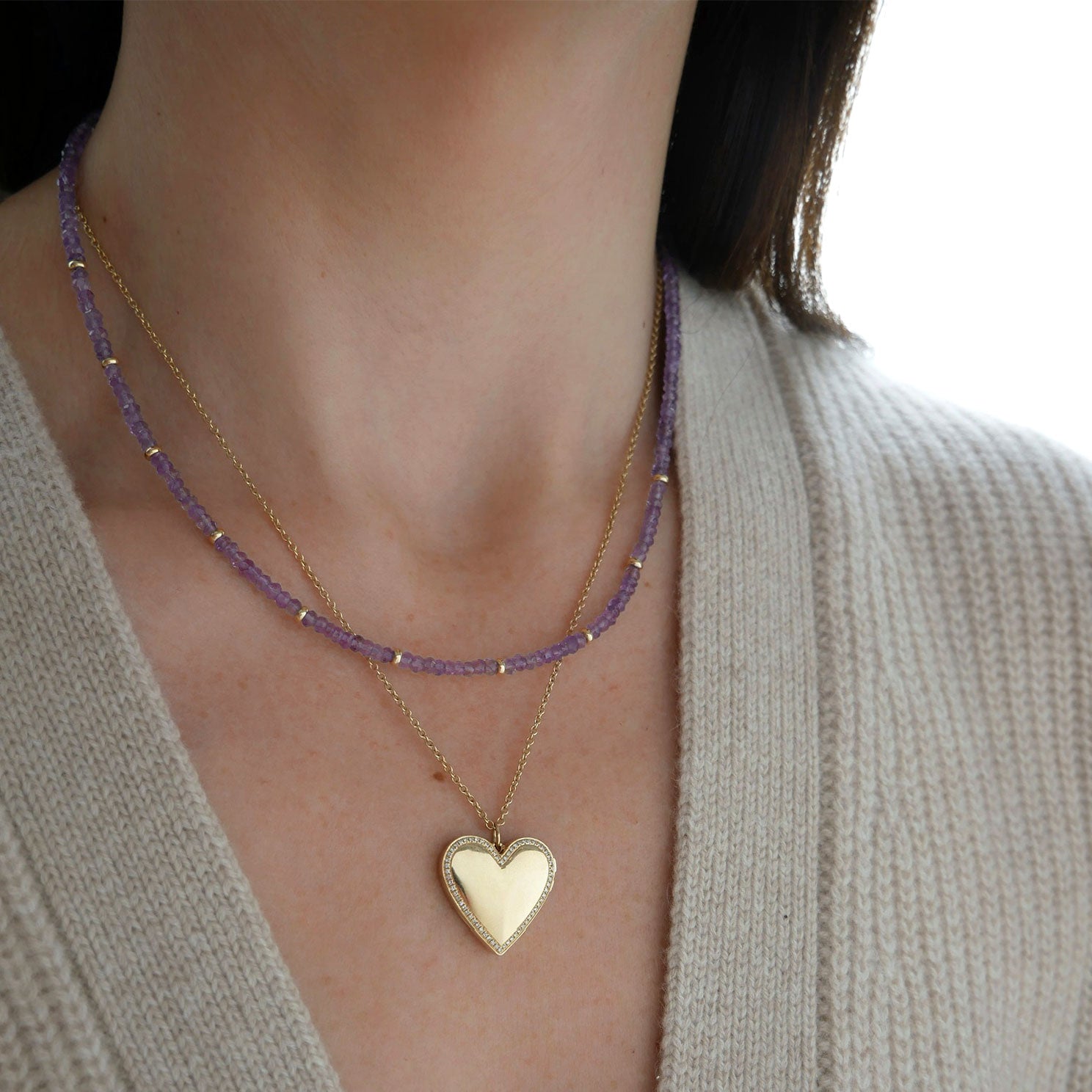 Birthstone Bead Necklace In Amethyst styled on neck of model with gold heart locket necklace and wearing tan sweater