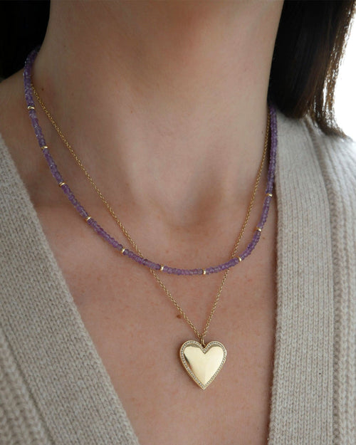 Birthstone Bead Necklace In Amethyst styled on neck of model with gold heart locket necklace and wearing tan sweater
