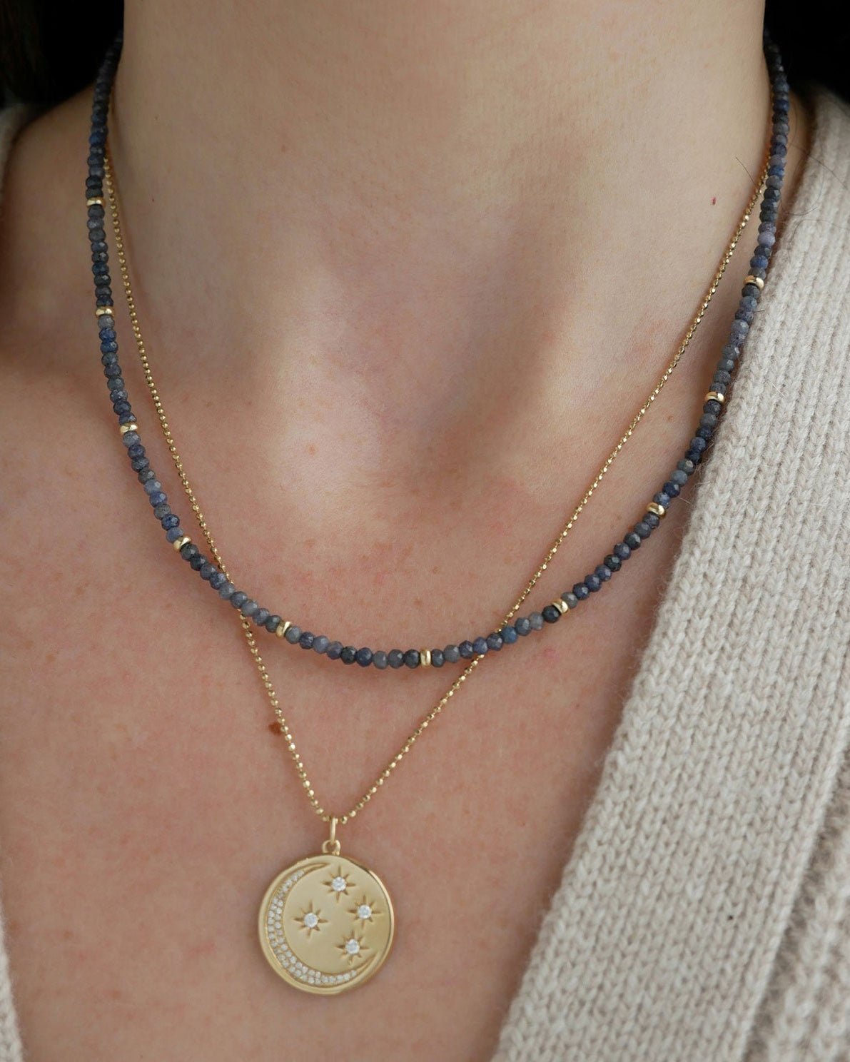 Birthstone Bead Necklace In Blue Sapphire styled on neck of model wearing gold celestial pendant necklace and wearing tan sweater
