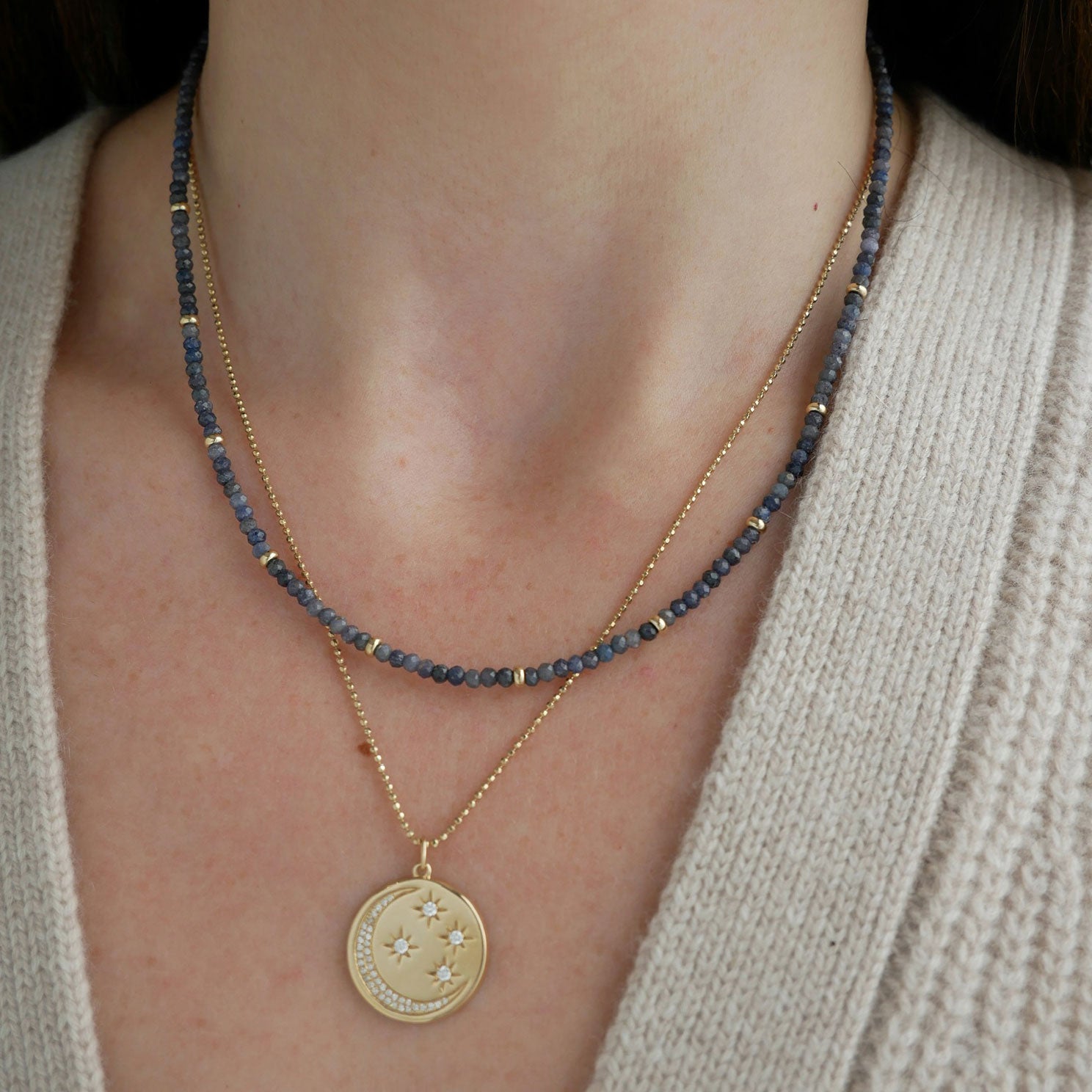 Birthstone Bead Necklace In Blue Sapphire styled on neck of model wearing gold celestial pendant necklace and wearing tan sweater