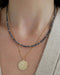 Birthstone Bead Necklace In Blue Sapphire styled on neck of model wearing gold celestial pendant necklace and wearing tan sweater
