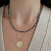 Birthstone Bead Necklace In Blue Sapphire styled on neck of model wearing gold celestial pendant necklace and wearing tan sweater