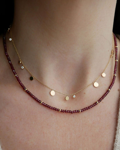 Birthstone Bead Necklace In Garnet styled on neck of model wearing diamond and gold confetti necklace and wearing tan sweater