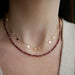 Birthstone Bead Necklace In Garnet styled on neck of model wearing diamond and gold confetti necklace and wearing tan sweater