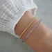 Birthstone Bead Bracelet In Amethyst styled on wrist with gold ball bracelet and wearing white sleeve