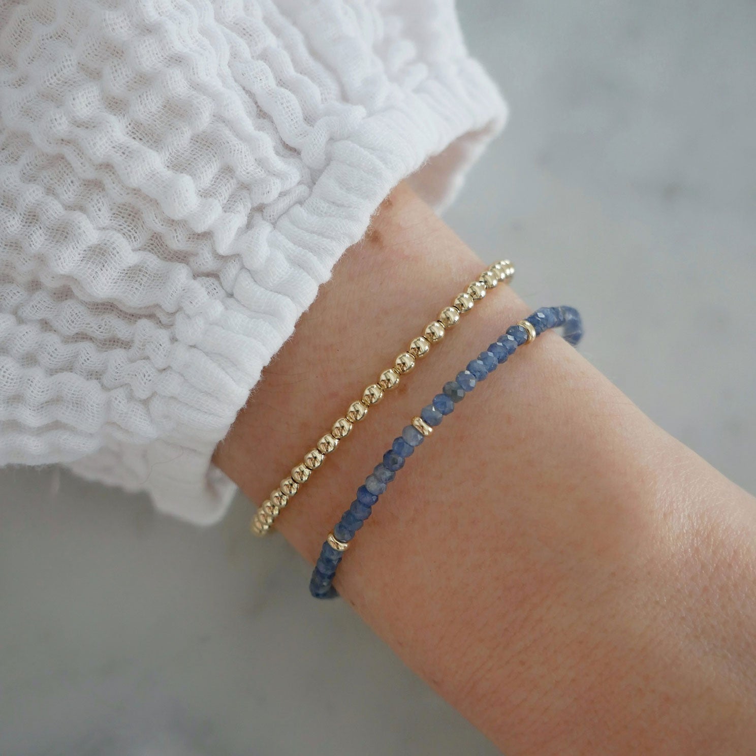 Birthstone Bead Bracelet In Blue Sapphire styled on wrist of model with gold ball bracelet wearing white sleeve