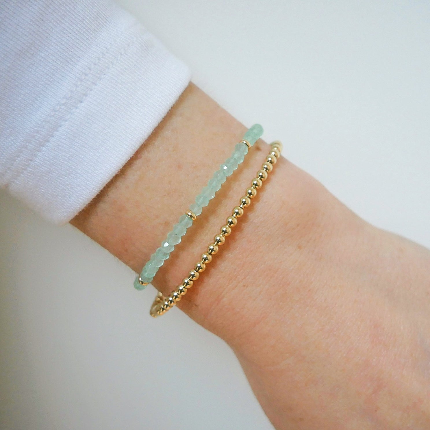 Birthstone Bead Bracelet In Chalcedony styled on wrist with gold ball stretch bracelet on model wearing white sleeve