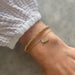 Birthstone Bead Bracelet In Diamond in 14k yellow gold styled next to angel wing bracelet on wrist of model with white sleeve