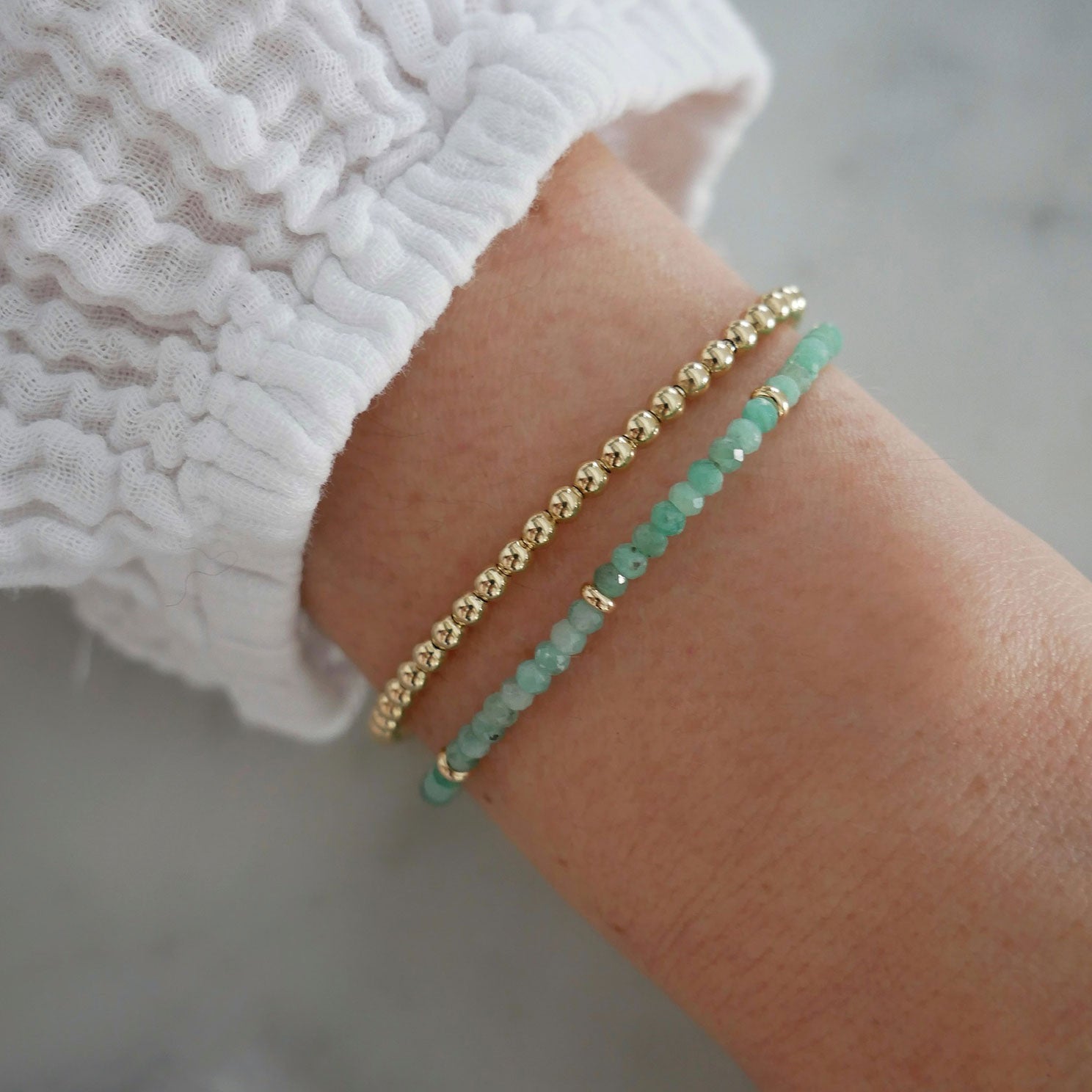 Birthstone Bead Bracelet In Emerald styled on wrist of model with gold ball bracelet and white sleeve