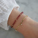 Birthstone Bead Bracelet In Garnet styled on wrist of model with gold chain bracelet and white sleeve