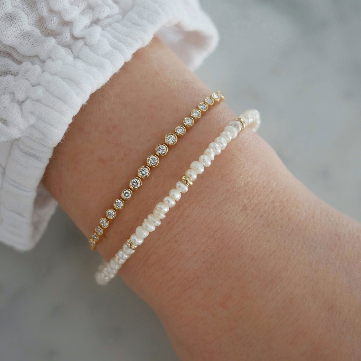 Birthstone Bead Bracelet In Pearl styled on wrist of model with diamond bracelet and wearing white sleeve