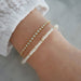 Birthstone Bead Bracelet In Pearl styled on wrist of model with diamond bracelet and wearing white sleeve