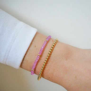 Birthstone Bead Bracelet in Pink Sapphire next to gold ball stretch bracelet styled on wrist of model wearing white sleeve