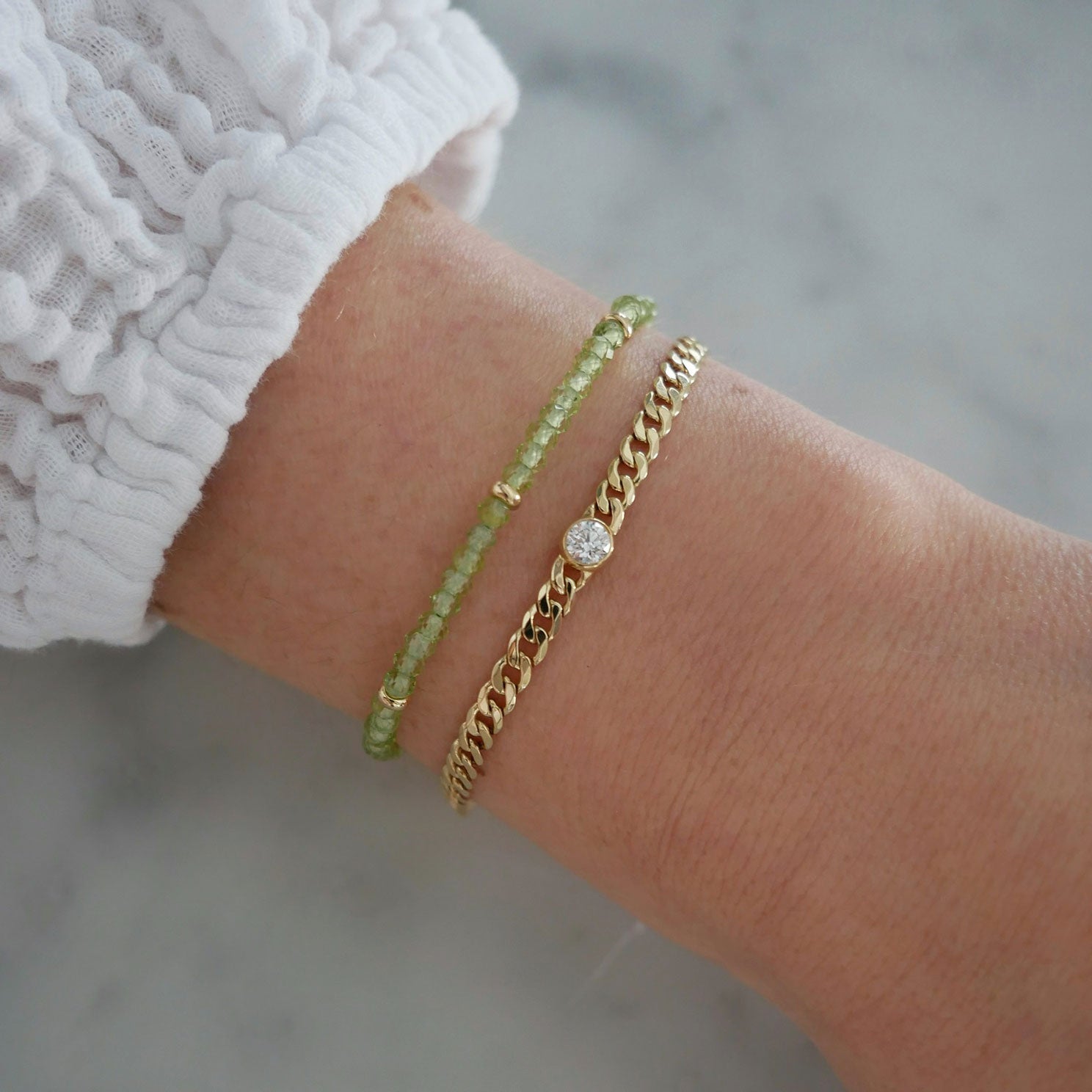 Birthstone Bead Bracelet In Peridot styled on wrist of model wearing diamond curb chain bracelet and white sleeve