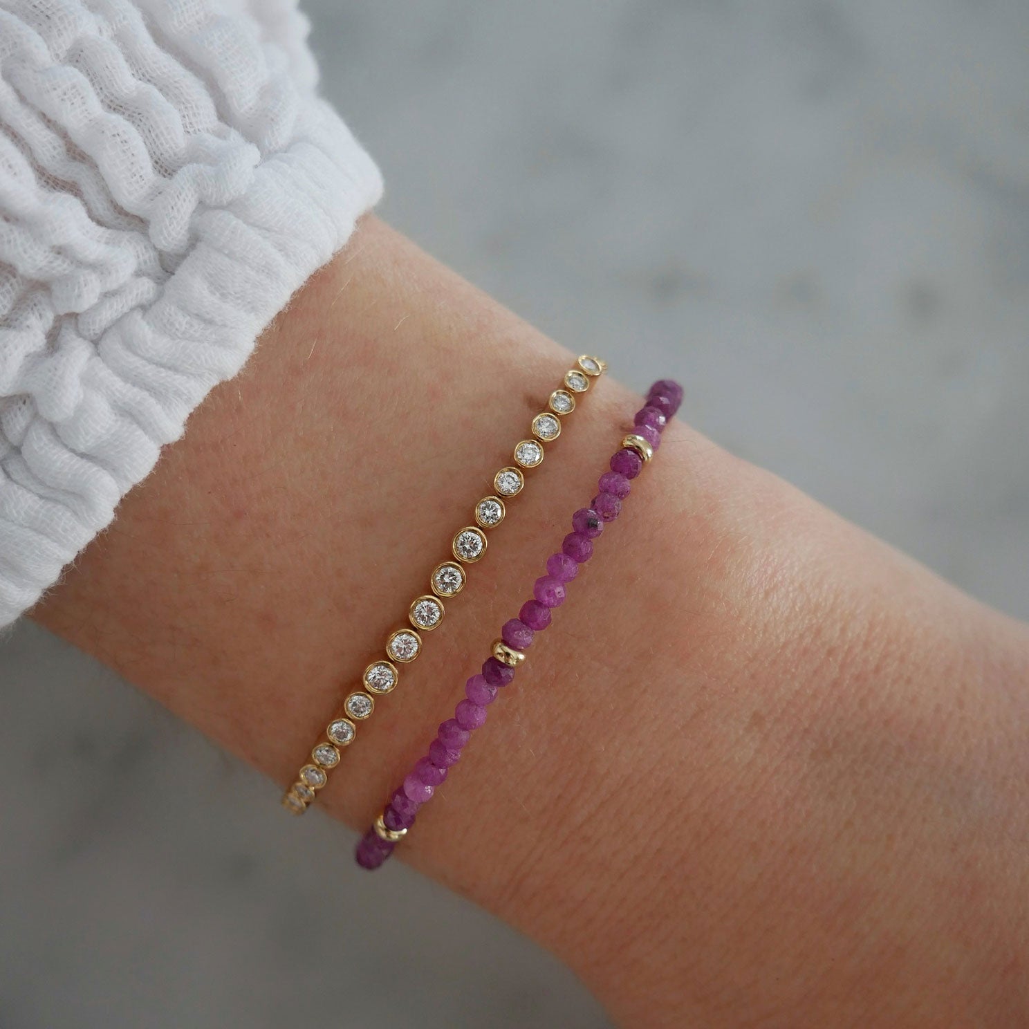 Birthstone Bead Bracelet In Ruby styled on wrist of model wearing diamond bracelet and white sleeve