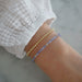 Birthstone Bead Bracelet In Tanzanite styled on wrist of model wearing gold ball bracelet and white sleeve