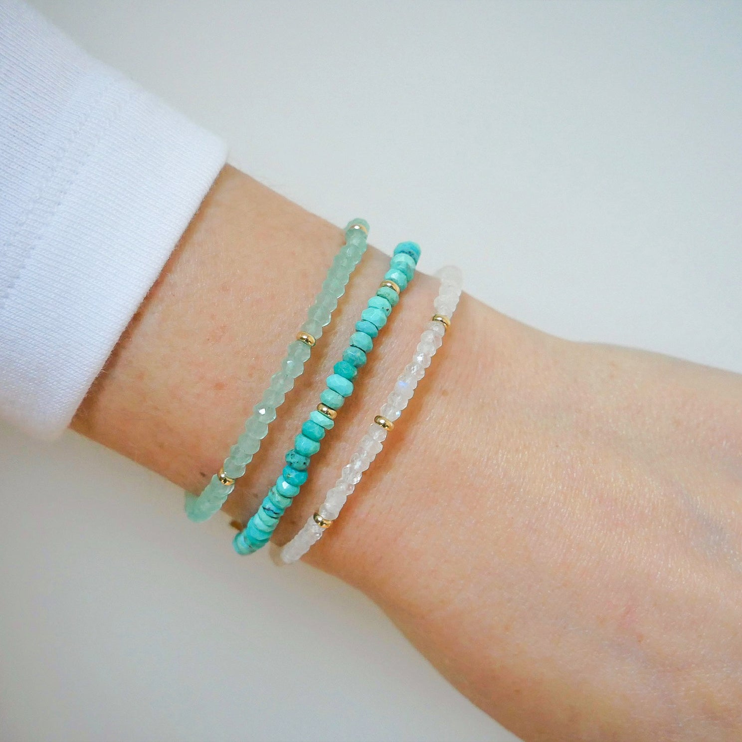 Birthstone Bead Bracelet In Moon Stone styled next to turquoise and labradorite bracelets styled on wrist with white sleeve