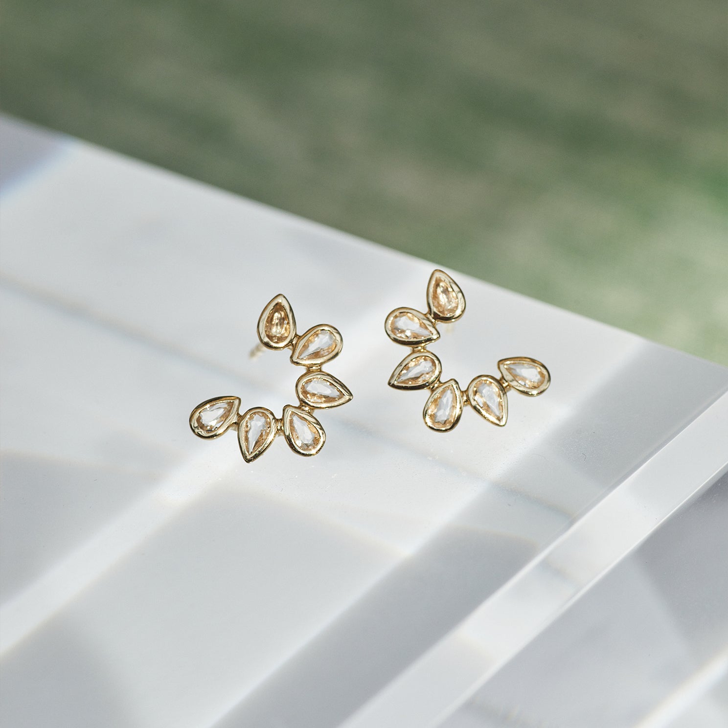 Multi White Quartz Pear Stud Earrings in 14k yellow gold sitting on top of white table