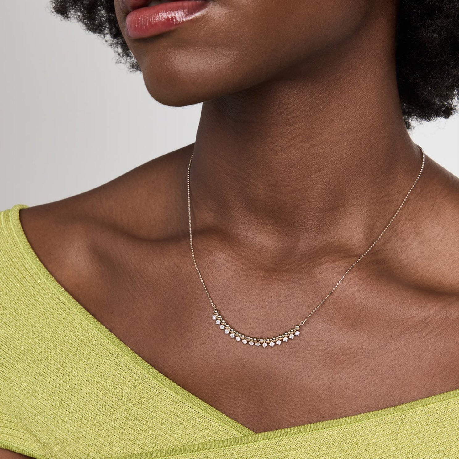 Diamond & Gold Ball Necklace in 14k yellow gold styled on neck of model wearing green top