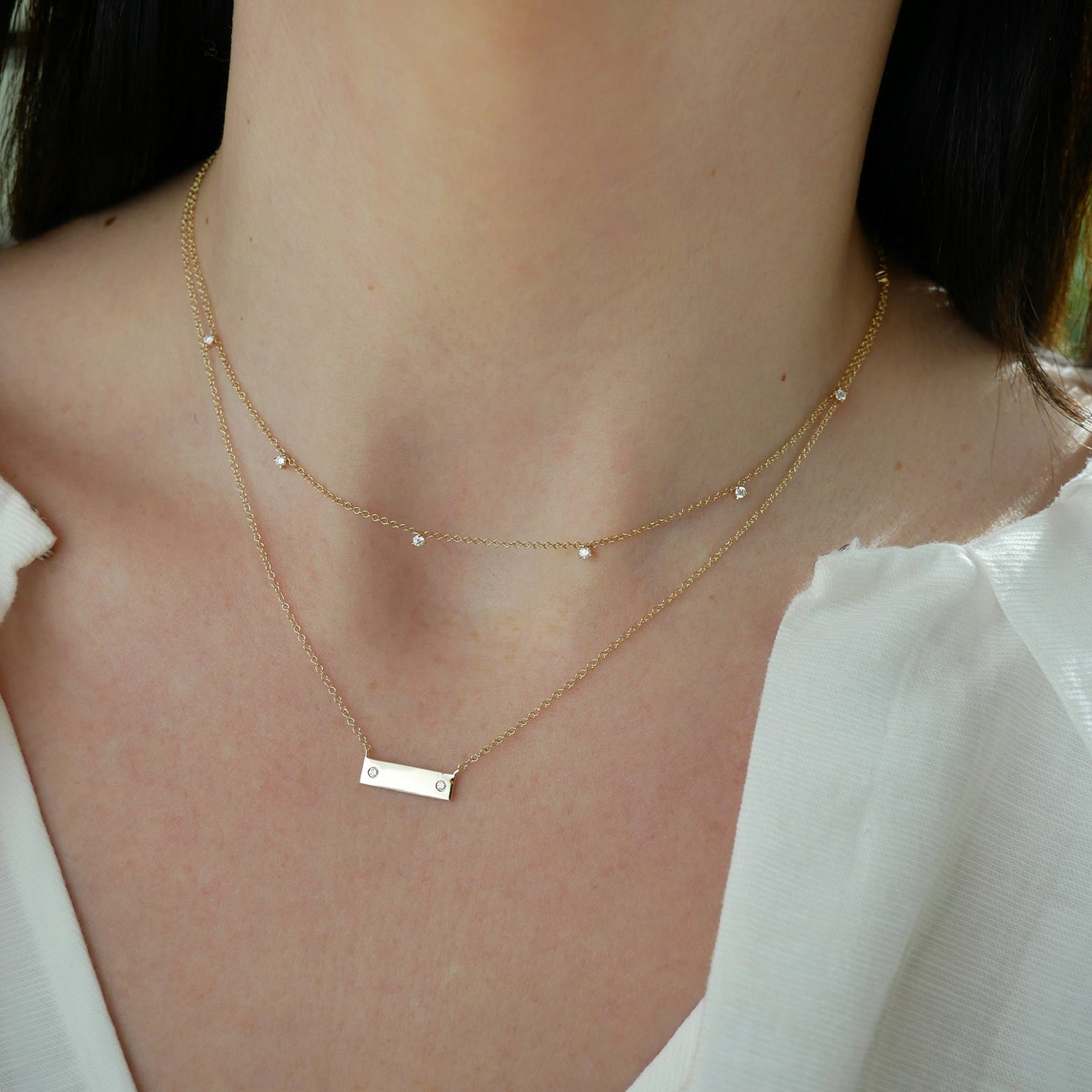 Mini Nameplate Necklace in 14k yellow gold layered with diamond prong set necklace styled on neck of model wearing white blouse