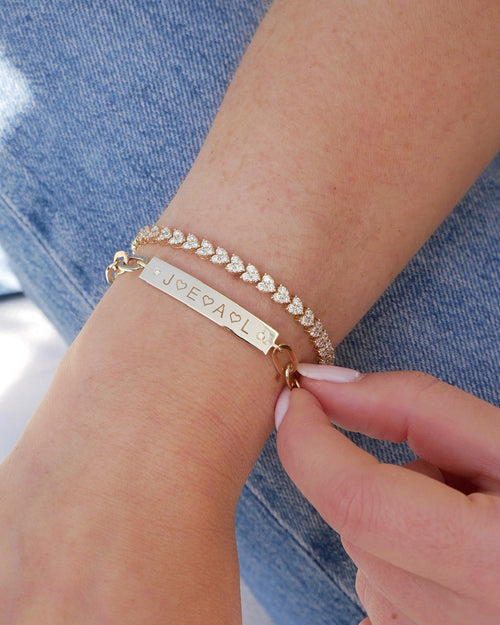 Nameplate Jumbo Link Bracelet in 14k yellow gold with engraving of J, E, A, L and four hearts styled next to endless love bracelet on wrist of model 