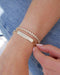 Nameplate Jumbo Link Bracelet in 14k yellow gold with engraving of J, E, A, L and four hearts styled next to endless love bracelet on wrist of model 