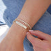 Nameplate Jumbo Link Bracelet in 14k yellow gold with engraving of J, E, A, L and four hearts styled next to endless love bracelet on wrist of model 