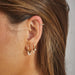 Pearl Shimmy Huggie Earring in 14k yellow gold styled on first earring hole of model next to huggie earrings with pearl drops