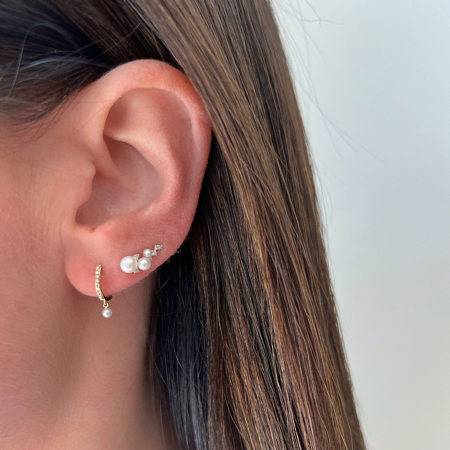 Diamond & Pearl Ear Climber in 14k yellow gold styled on second earring hole on ear lobe of model next to diamond mini huggie with pear drop