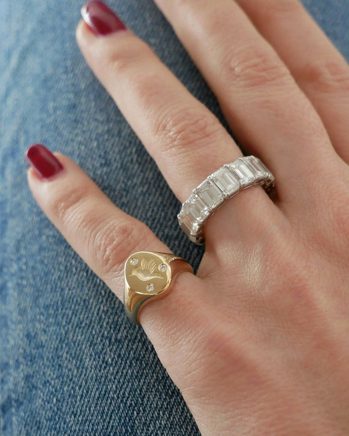 Diamond Hummingbird Signet Ring in 14k yellow gold styled on pinky ring next to emerald cut ring on ring finger both rings styled on fingers of model