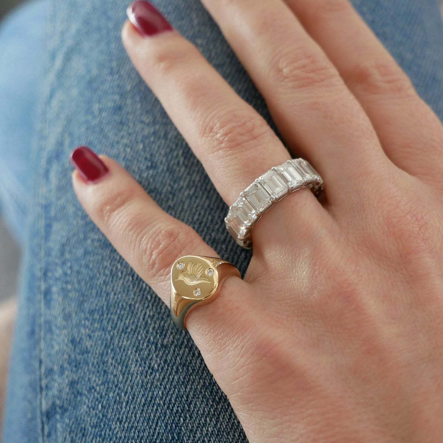 Diamond Hummingbird Signet Ring in 14k yellow gold styled on pinky ring next to emerald cut ring on ring finger both rings styled on fingers of model