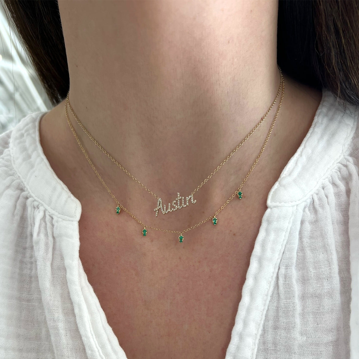 Emerald 5 Teardrop Choker Necklace in 14k yellow gold layered with custom script necklace in Austin both necklaces styled on neck of model wearing white blouse