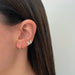 Diamond Flutter Stud Earrings in 14k yellow gold next to diamond mini huggie with emerald drop both earrings styled on ear lobe of model with brown hair