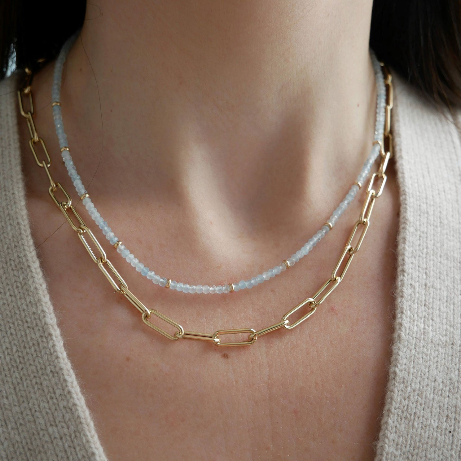 Birthstone Bead Necklace In Aquamarine styled on neck of model with gold jumbo chain necklace and wearing tan sweater