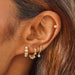 Diamond Mini Huggie With Diamond Bezel Drop Earring in 14k yellow gold style don third earring hole on earlobe of model with two huggie earrings on first and second earring hole and one cartridge piercing